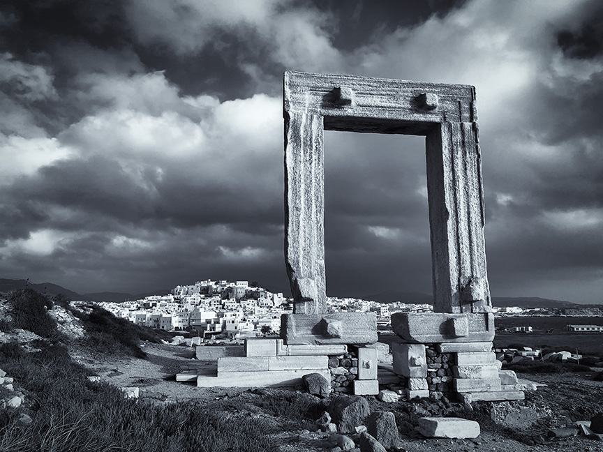 Black and white image of the great ancient arch at the mouth of Naxos Harbor in Greece.