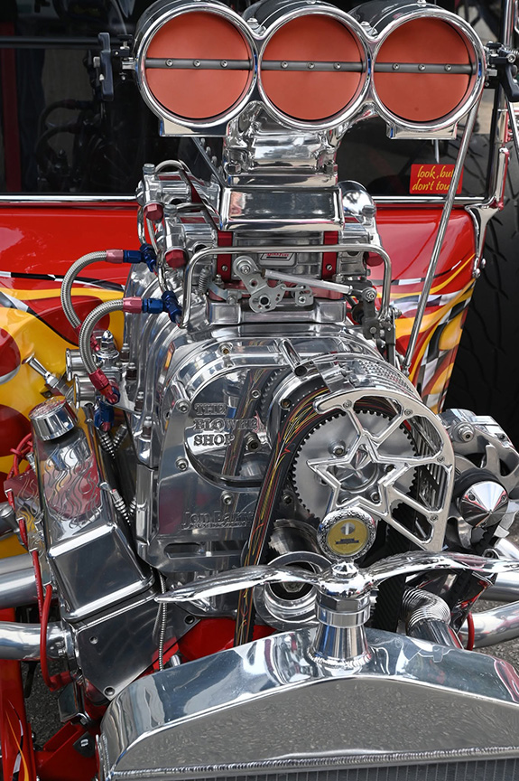Elaborately built-out engine from the street rod at the top of the article, featuring a big triple intake,  sinuously curving exhaust pipes, and an awful lot of spotless stainless steel.